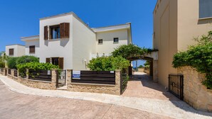 A residential street with white buildings, stone walls, and a sign indicating 'Villa Greco Monte 24'. - Villa Greco Mare #5 (Paralimni)