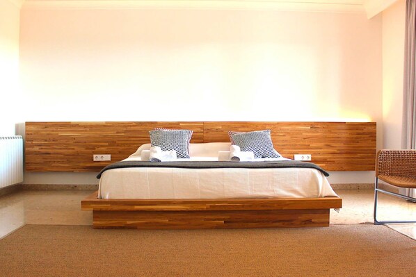 A modern bedroom with a wooden headboard, a bed with white bedding, and two patterned pillows.