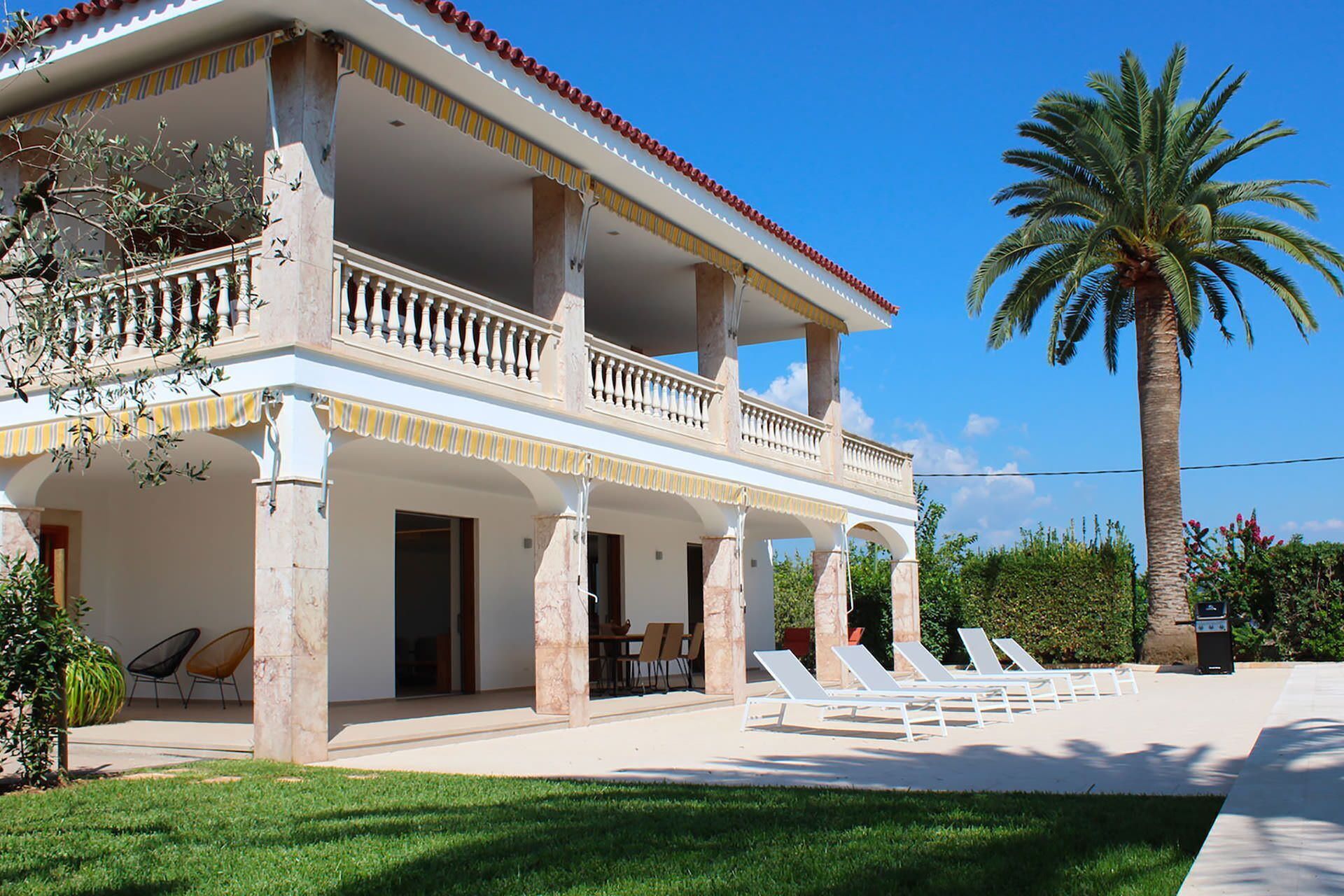 A two-story building with a balcony, outdoor seating, and a palm tree.
