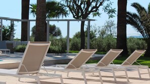 A row of beige lounge chairs with white frames, arranged on a paved patio with a pergola overhead. - My Rental Homes - Villa Acapulco private pool, barbeque and wifi (Palma De Mallorca)