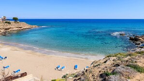 A beach with clear blue water, sandy shore, and blue lounge chairs. - Royal Beachfront Villa (Paralimni)