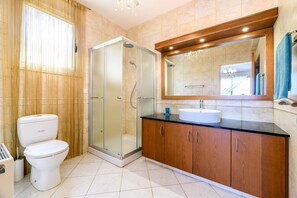 Une salle de bain comprenant des toilettes, une douche fermée par une paroi de verre, un lavabo et un miroir.