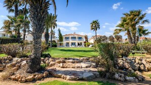 A large house with a well-maintained lawn, palm trees, and a rock garden. - Royal Beachfront Villa (Paralimni)