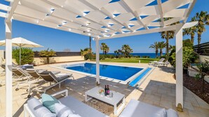 A poolside area with a pergola, lounge chairs, and a pool. - Royal Beachfront Villa (Paralimni)