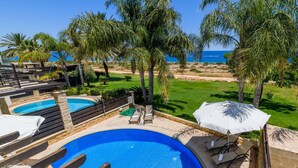 A pool area with two pools, lounge chairs, and umbrellas. - Villa Greco Mare #6 (Paralimni)