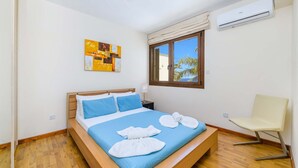 A neatly made bed with blue bedding, a wooden headboard, and a pair of white towels. - Villa Greco Mare #6 (Paralimni)