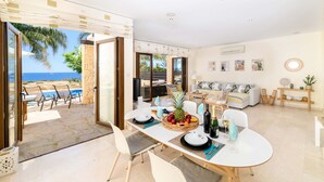A spacious living area with a dining table set for four, a sofa, and a view of the sea. - Villa Greco Mare #6 (Paralimni)