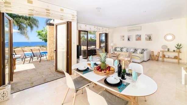 A spacious living area with a dining table set for four, a sofa, and a view of the sea. - Villa Greco Mare #6 (Paralimni)
