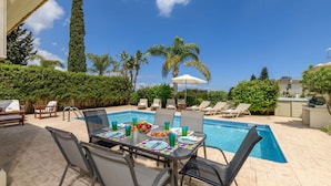 Un espace extérieur avec une piscine, une table dressée pour les repas, des chaises longues et un barbecue.