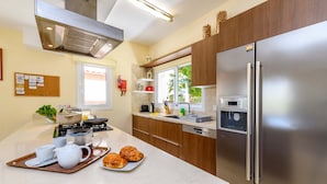 Une cuisine moderne dotée d’appareils électroménagers en acier inoxydable, de meubles en bois et d’un grand îlot central où sont disposés des aliments pour le petit-déjeuner.