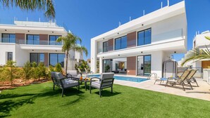 Ein modernes, zweistöckiges Haus mit Pool, Sitzgelegenheiten im Freien und einem gepflegten Rasen.
