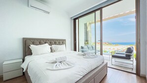 A modern bedroom with a large bed, a glass door leading to a balcony with a view of the beach. - Azure Seaview - Jade Villa (Paralimni)
