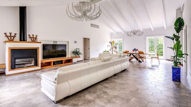 Amplia sala de estar con un sofá blanco grande, una chimenea, un televisor y un comedor con mesa y sillas.