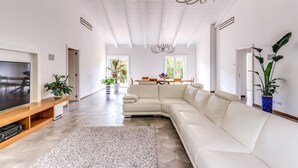 Un salón amplio con un sofá modular grande, un televisor y un comedor con mesa y sillas.