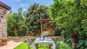 Un patio con una mesa lista para comer, rodeado de abundante vegetación y una pérgola.