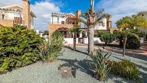 A residential area with houses, a palm tree, and a garden with various plants. - Villa Anna Maria (Sotira)