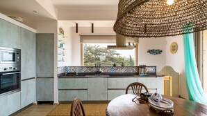 Una cucina moderna con elettrodomestici integrati, una zona pranzo con tavolo in legno e un'ampia finestra che si affaccia sul verde.