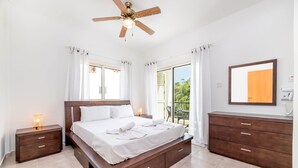 A bedroom with a bed, a nightstand, a dresser, a ceiling fan, and a view of the outdoors. - Pernera Blue Villa (Paralimni)