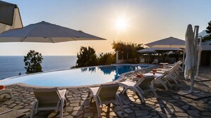 Ein Poolbereich mit Liegestühlen und Sonnenschirmen mit Blick aufs Meer.