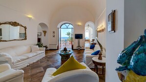 Ein geräumiges Wohnzimmer mit weißen Sofas, einem Couchtisch und Meerblick durch bogenförmige Fenster.