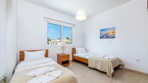 A hotel room with two beds, a window with a view, a painting on the wall, and a lamp. - Villa Amesta (Paralimni)