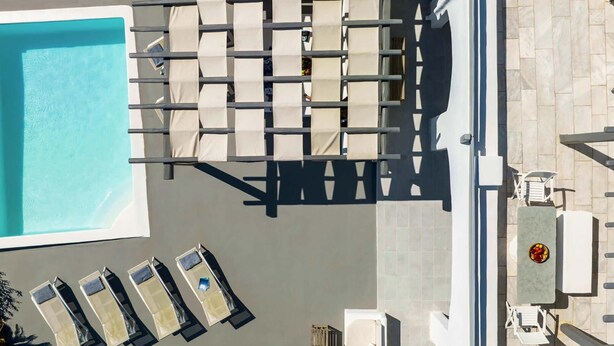 An aerial view of a pool area with a rectangular pool, multiple lounge chairs, and a small table with a bowl of fruit. - Villa Apollonia with pool and sea view (Mykonos)