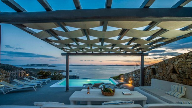 A covered outdoor area with a pool, lounge chairs, and a stone wall.