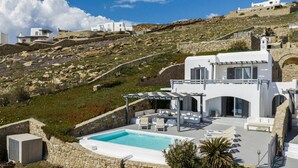 A white villa with a pool, stone walls, and a view of the surrounding landscape.