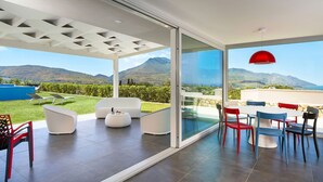 Un patio moderno al aire libre con pared de vidrio, mobiliario blanco y una lámpara colgante roja.