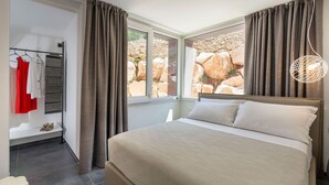 Un dormitorio con cama, ventana con cortinas, lámpara colgante y un perchero con una prenda roja.
