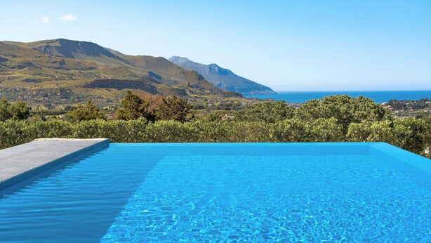 Piscina infinita azul cristalina con vistas a un paisaje montañoso y al mar.