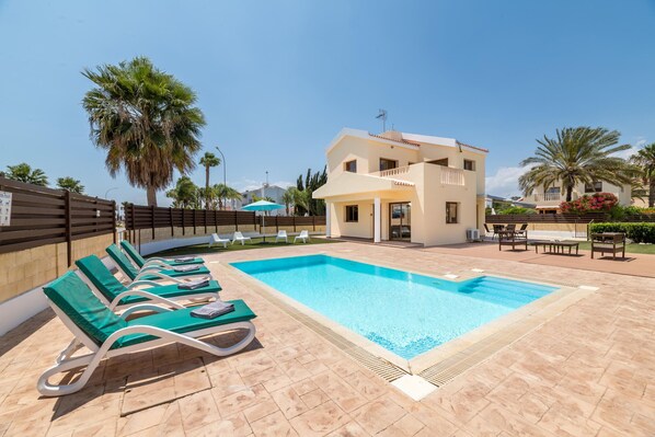 A pool area with lounge chairs and a two-story building in the background. - Villa Sarah (Sotira)