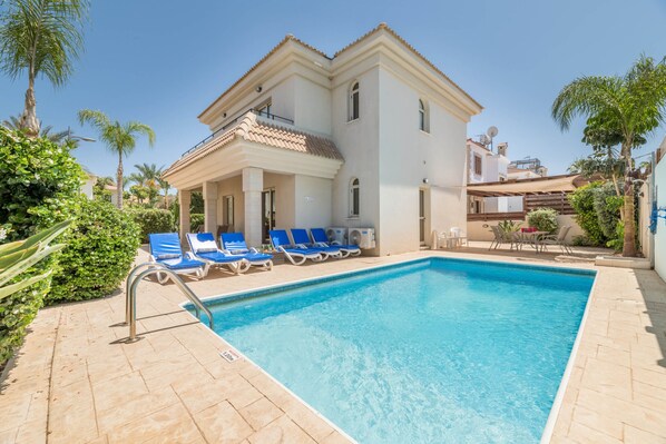 Un edificio a due piani con una piscina, poltrone da relax blu e palme.