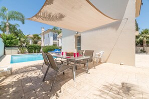 Una terrazza esterna con piscina, un tavolo e sedie, e un'ampia vela parasole.