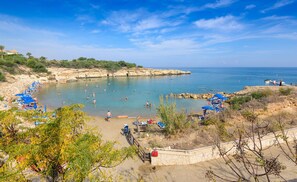 Una spiaggia con acque cristalline, persone che nuotano e ombrelloni.