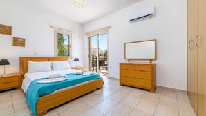A modern bedroom with a wooden bed, a nightstand, a dresser, and an air conditioning unit. - Villa Lindo (Paralimni)