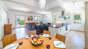 A spacious living area with a dining table set for a meal, a kitchen with modern appliances, and a large chandelier. - Villa Lindo (Paralimni)