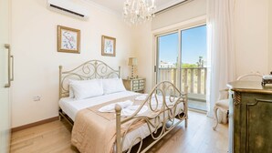Un dormitorio con cama, cómoda, silla, balcón con vistas y candelabro.