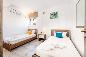Een hotelkamer met twee bedden, een raam met uitzicht, een airconditioning, een nachtkastje met een lamp en een schilderij aan de muur.