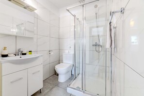 Een moderne badkamer met een douchecabine van glas, een wit wastafelmeubel en een toilet.