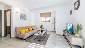A modern living room with a sofa, coffee table, TV, and plants. - Napa Centro Apartment (Ayia Napa)