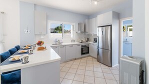 A modern kitchen with white cabinets, a central island, and stainless steel appliances. - Nemea Serenity Blue (Ayia Napa)