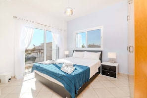 A bedroom with a bed, a nightstand, a window, and a balcony. - Nemea Serenity Blue (Ayia Napa)