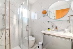 A modern bathroom with a glass-enclosed shower, a toilet, and a vanity with a mirror and toiletries. - Nemea Serenity Blue (Ayia Napa)