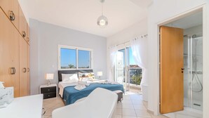 A bedroom with a bed, a bedside table, a nightstand, a bathroom with a shower, and a balcony with a view. - Nemea Serenity Blue (Ayia Napa)