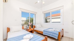 Hotellihuone, jossa on kaksi erillistä sänkyä, pieni pöytä maljakolla ja ikkuna, josta on näkymä ulos.