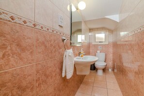 A bathroom with pink marble tiles, a white sink, a toilet, and a towel hanging on a rack. - Villa Maria (Paralimni)
