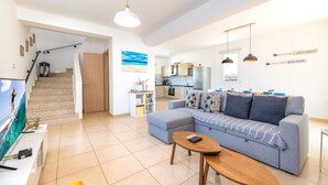 A modern living room with a sofa, coffee table, and TV. There is a staircase leading to another room. - Villa Kohili (Paralimni)