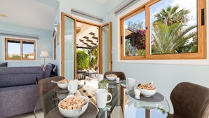 Un comedor con una mesa de vidrio, tazones de cereal y vistas a palmeras afuera.