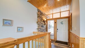 Un escalier en bois mène à une pièce dont un des murs est en pierre, avec une porte blanche et des tableaux encadrés accrochés au mur.